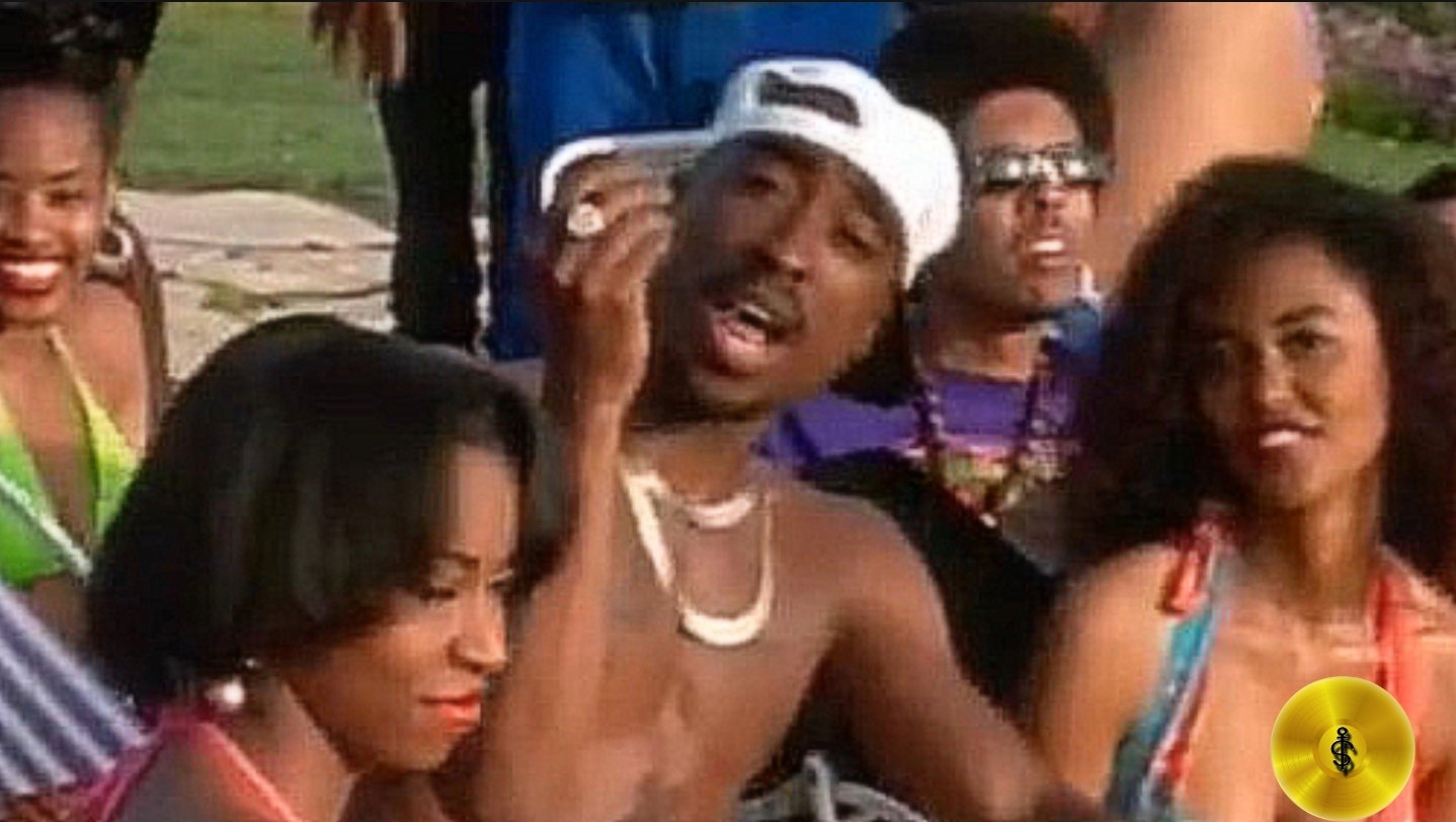 A picture of 2pac in a music video beside girls